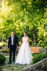 Beautiful couple walking in the park in their wedding day. Sunny weather.