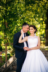 Beautiful couple walking in the park in their wedding day. Sunny weather.