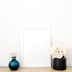 Front view blank mock up of photo frame with flowers at white background. Minimalistic decorated home office concept.