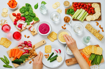 Women's hands and variation of healthy vegan snacks. Vegetables, crackers, dip and hummus
