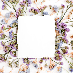 Empty white paper blank on blue and purple dried flowers frame on white background. Flat lay, top view