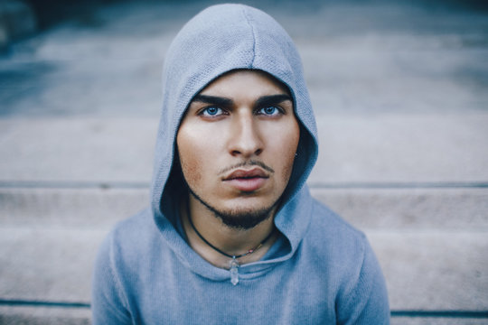 Conceptual art portrait of spooky weird beautiful handsome young middle east brunette blue eyes man face with beard, wearing blue hoodie, looking in camera