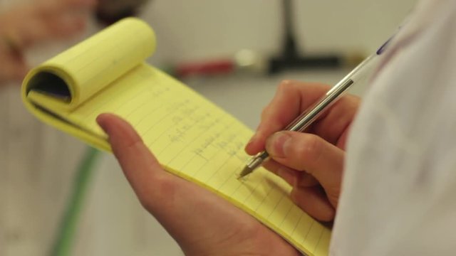 Hand writes on a yellow block pad