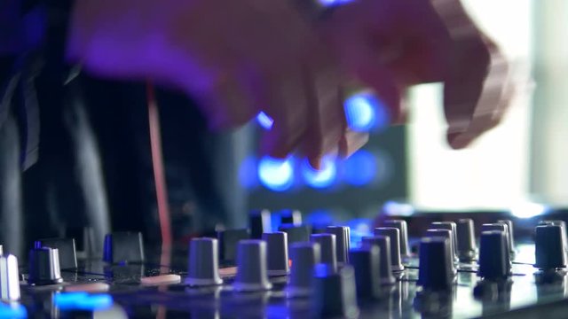 Club DJ hands tweak track controls on dj's deck. 4K.