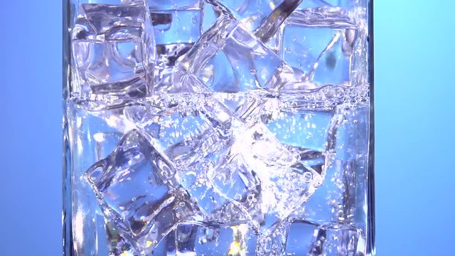 Water is pouring into a glass with ice cubes. Clear water pours ice cubes on a blue  background. Pure water  with Ice and bubbles in glass. Full HD  footage 1920x1080p. Slow motion 240 fps