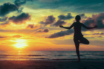 Meditation yoga silhouette of woman on Ocean beach at surreal sunset.