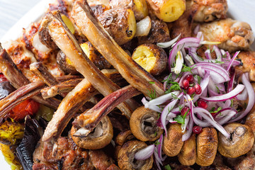 Fototapeta premium Meat plate with delicious pieces of meat, ribs, grilled potatoes and mushrooms with onion and pomegranate grains. Close up image with selective focus