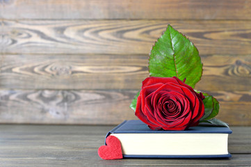 Mothers Day gift. Red rose, heart and book on wooden background