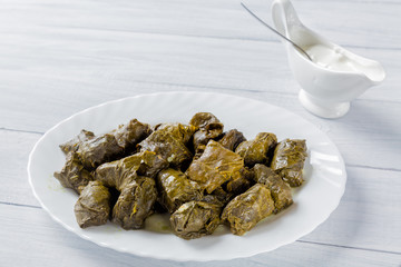 Dolma stuffed meat in grape leaves on white plate and bowl with cream sauce on white wooden table