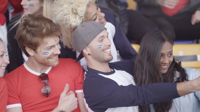  Friends sitting in the crowd at sports event pose to take a selfie with phone