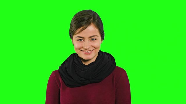 A young modest lady smiling and closing her eyes against a green background. Medium shot
