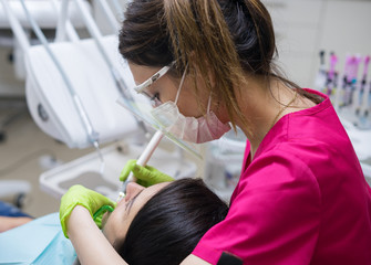 Female dentist cleaning teeth of a beautiful patient woman in dental clinic - obrazy, fototapety, plakaty