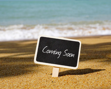 Coming soon text written on blackboard with blue ocean background.
