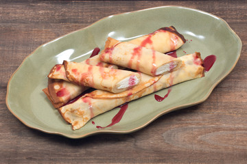 Delicious cheese blintz with raspberry syrup on green plate and wooden vintage tray