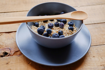 Oat flakes with blueberry in a blue cup on a wooden table.