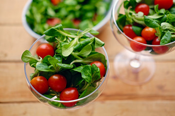 Cherry tomatoes and basil salad on a glass cup on a wooden table.