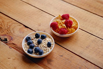 Golden corn flakes, Hercules oat and some berries in a cup on a wooden table.