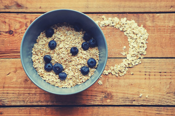 Oat flakes with blueberry in a blue cup on a wooden table.