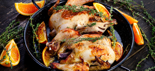 Roasted two chicken with oranges and thyme on a dark wooden background.