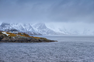 Travel and Tourism Concepts. One Separate House on Seashore Coastline in Norway Against Mountains Covered With Snow.