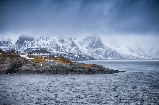 Travel and Tourism Concepts. One Separate House on Seashore Coastline in Norway Against Snowy Mountains.