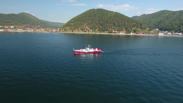 Red Ship sails along oldest Baikal port. Russia Siberia Listvyanka village. Tourists on the ship. Green mountains pine forest. Best beautiful Sunny summer day. Unique aerial flight around 4k