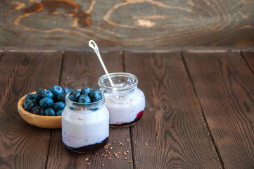 Berry yoghurt with flax seeds and jam in a small jar, blueberries in a plate on a wooden background. Healthy eating concept.