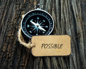 Compass and paper tag written with POSSIBLE on wooden background.