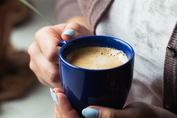 Girl with blue manicure holds a blue cup of coffee