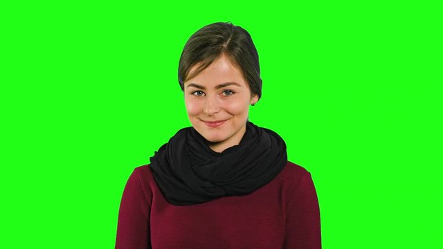 A pretty young modest lady smiling and pointing her finger against a green background. Medium shot