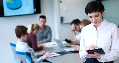 Portrait of  smiling casual businesswoman using tablet  with coworkers standing in background