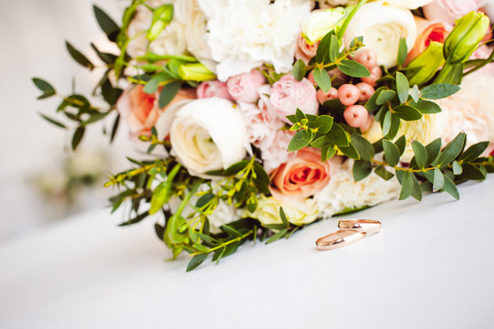Photo image of a classic wedding gold rings of the bride and groom on a white table, with a beautiful wedding bouquet of flowers of the bride