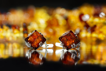 Closeup silver earrings rhombus with authentic natural baltic amber on black  surface on background of orange amber