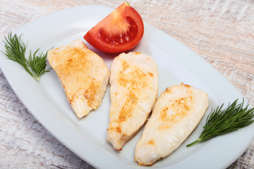 Slices of roasted chicken breast and tomato on white plate