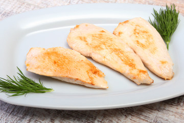 Slices of roasted chicken breast and tomato on white plate