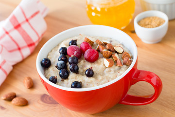 Oatmeal porridge with black currant, cranberries and almonds served in bowl. Honey and holden linseeds on side