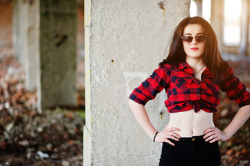 Portrait girl with red lips wearing a red checkered shirt, sunglasses with bare belly background abadoned place.