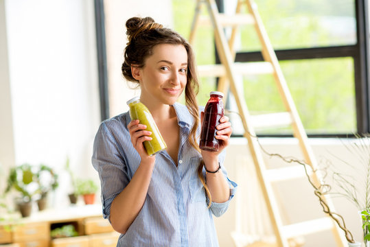 Portait of a beautiful happy woman with smoothie drinks in bottles at home. Healthy drinks concept