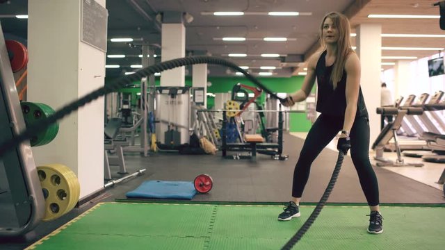 Young attractive woman with battle ropes exercise in the fitness gym and crossfit center