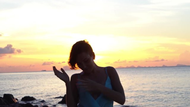 Happy young woman in a long dress dancing on the beach on a colourful sunset background
