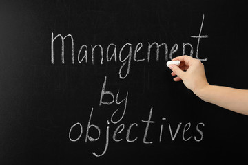 Female hand writing text MANAGEMENT BY OBJECTIVES on chalkboard