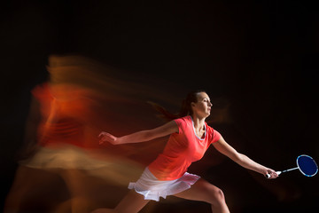 Young woman playing badminton over black background
