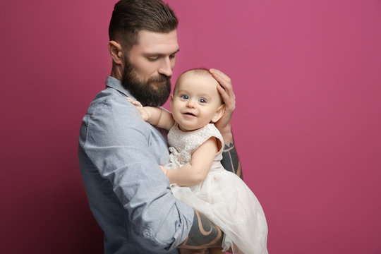 Handsome tattooed young man holding cute little girl on color background