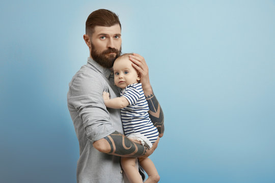 Handsome tattooed young man holding cute little baby on light background