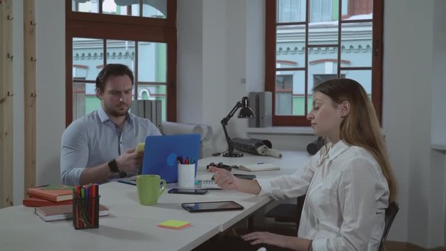 people waiting news in the office. Adult caucasian manager checking email using smartphone. Attractive businesswoman sitting at the working place with anxiety looking on coworker.