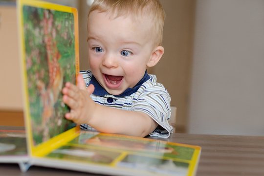 Baby boy turns the page in the book with animal. He is very happy and excited by watching pictures. Child concept.