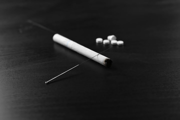 Acupuncture needles with cigarette on dark background