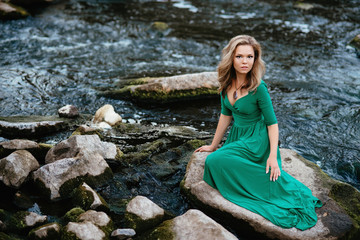 Beautiful girl posing on rocks near the water. Model in a green dress in nature.