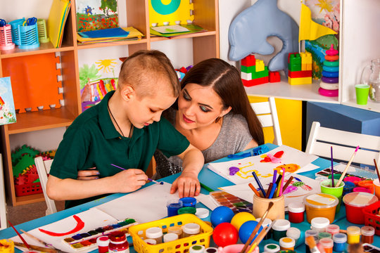 Small students girl and boy with teacher painting in art school class. Child drawing by paints on table. Mom praises son in kindergarten. Craft drawing education develops creative abilities of