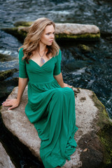 Beautiful girl posing on rocks near the water. Model in a green dress in nature.